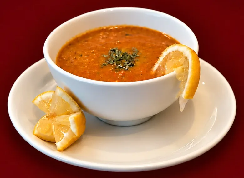 A bowl of Persian soup with dried herbs and lemon wedges